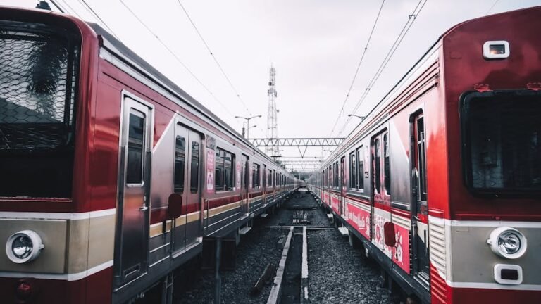 Dynamic shot of two red trains facing each other at a railway station under cloudy skies.