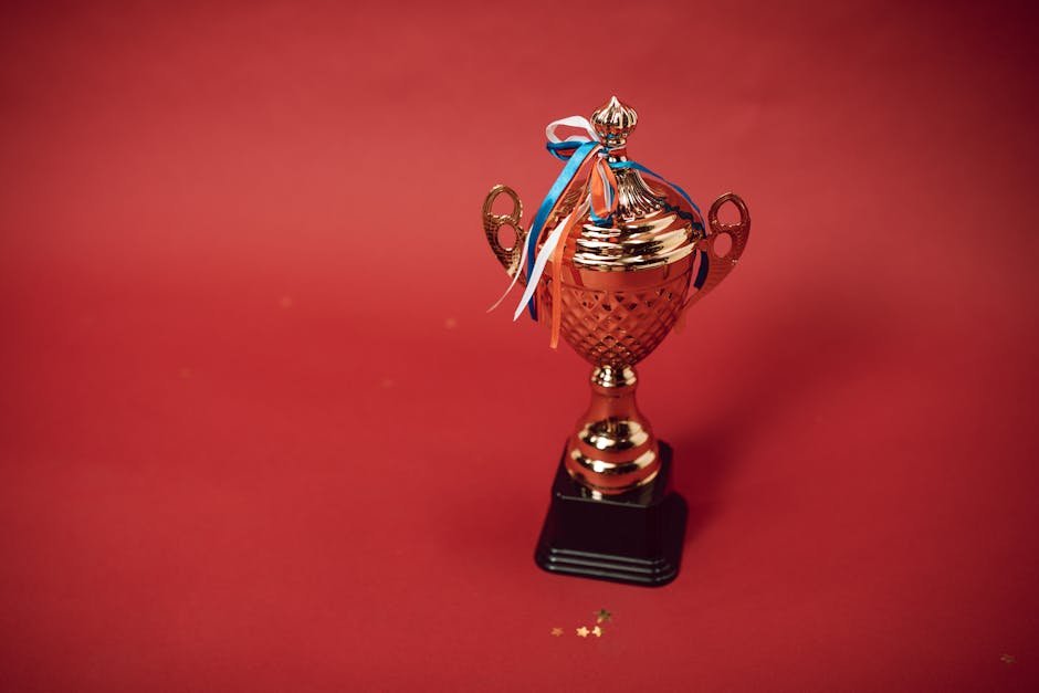 Golden trophy cup with red, blue, and white ribbons on a red backdrop symbolizes achievement and success.
