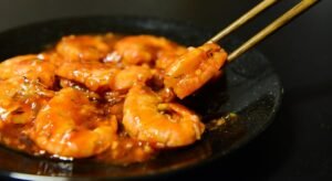 Close-up of spicy prawns in sauce with chopsticks on a dark plate