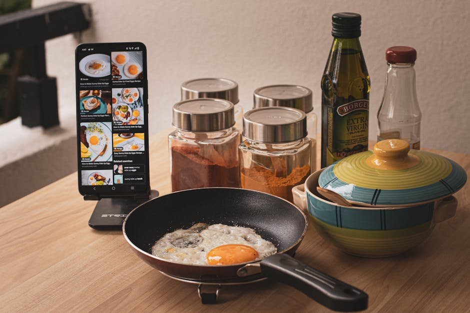 Fried egg cooking with smartphone recipe guidance, spices and ingredients on a kitchen counter.