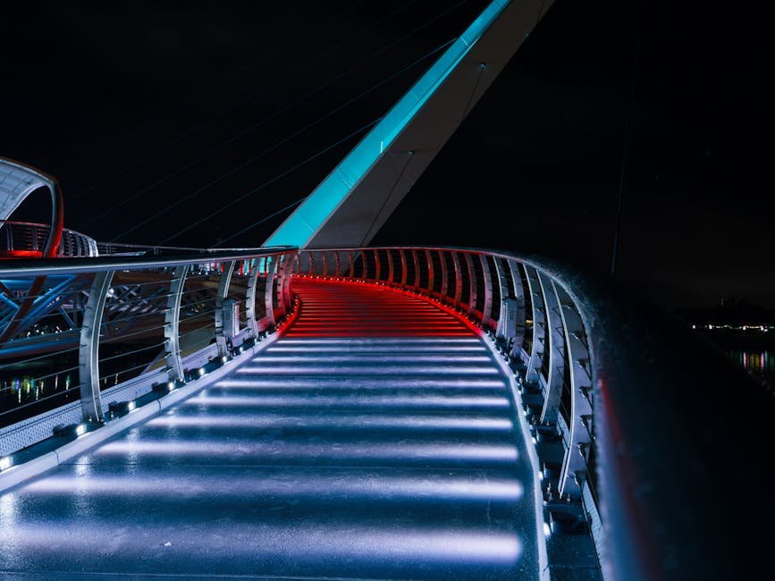 Curved modern bridge illuminated with vibrant red and blue lights at night.