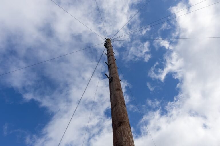 Wooden utility pole with wires extending in a cloud-dappled blue sky.