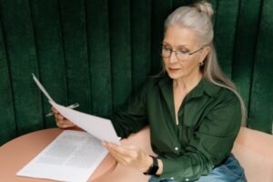 Senior woman wearing glasses, reading documents at a desk indoors, showcasing professional focus.