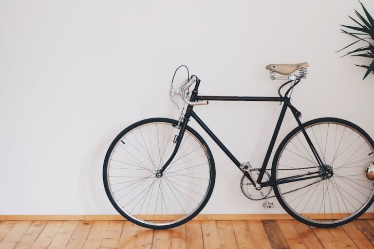 A vintage-style bicycle leaning against a clean white wall with wooden flooring, emphasizing minimalist design.