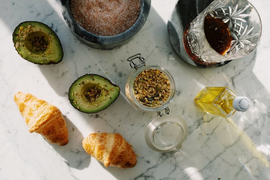 Flat lay of a nutritious breakfast setup with avocado, croissants, and seeds on marble.