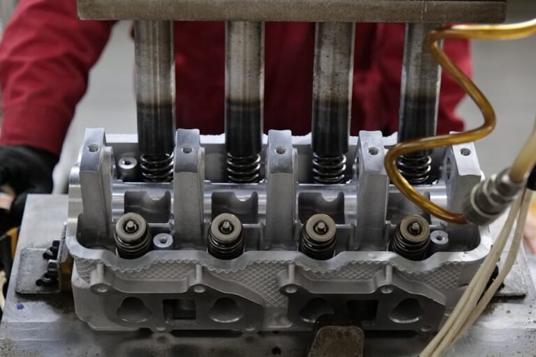 Detailed view of a metallic engine cylinder head with springs and pistons, assembled in an industrial workshop.