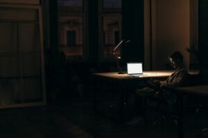 A man working late at night in a dimly lit office, with a bright laptop screen.