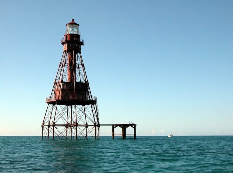 A towering metal lighthouse stands isolated in the ocean under a clear sky.