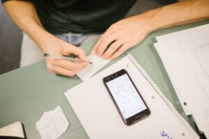 Close-up of student writing notes with a phone displaying diagrams. Concept of study aids and education.