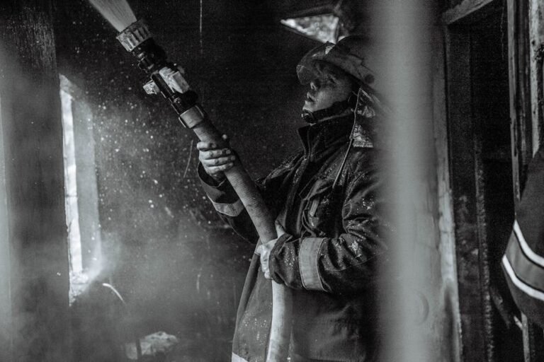 A determined firefighter battles smoke and flames with a hose in this monochrome scene.