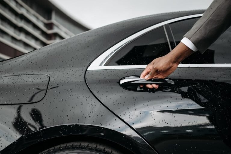 A close-up of a hand opening a black car door covered in raindrops, showcasing elegance and weather detail.