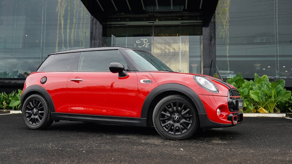 Red Mini Cooper parked outside modern building on rainy day.