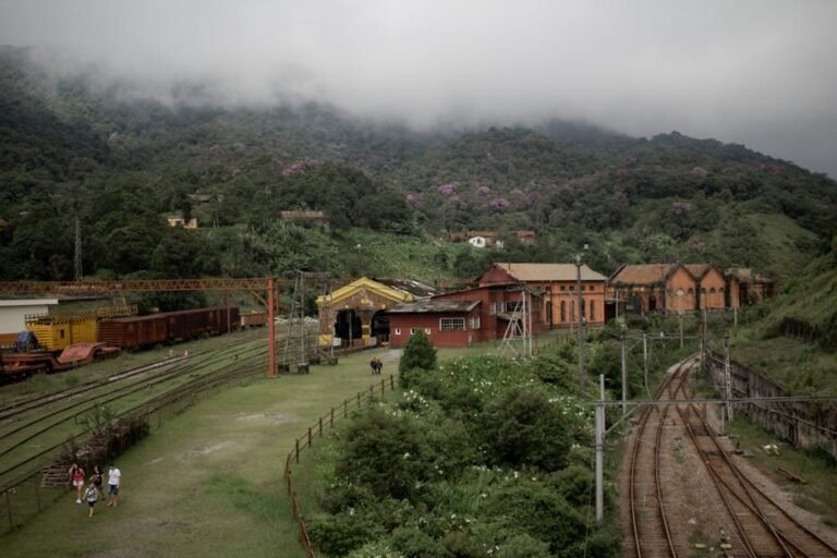 Aerial view of a historic railway station surrounded by lush green hills and misty mountains.