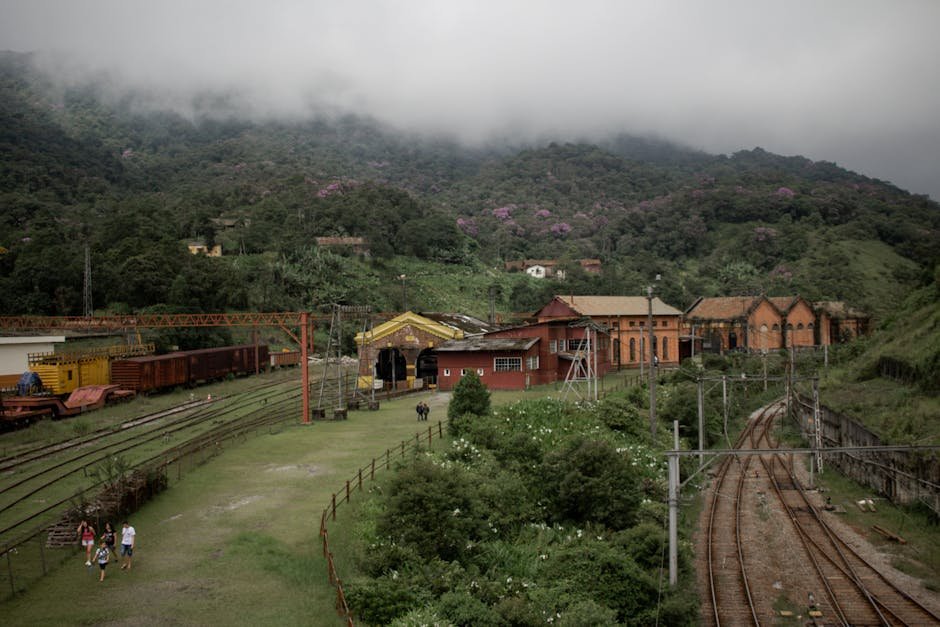 Aerial view of a historic railway station surrounded by lush green hills and misty mountains.